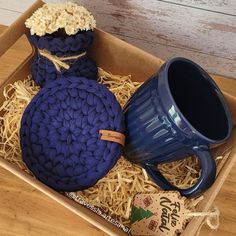 a blue coffee mug sits in a box next to a crocheted pot cozy