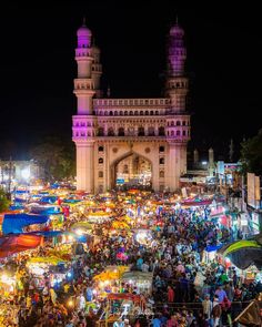 an outdoor market with lots of umbrellas and people walking around it at night time