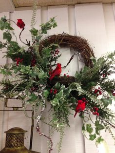 a wreath with red roses and greenery is hanging on the wall next to a lantern