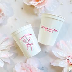 two coffee cups sitting next to each other on a table with flowers in the background