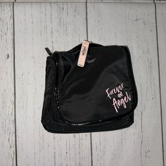 a black purse with pink writing on the front and side, sitting on a white wooden floor