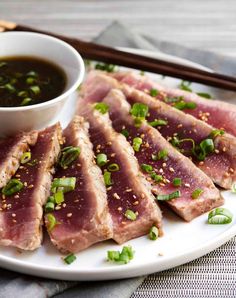 grilled tuna steaks served on a white plate with dipping sauce and green onions