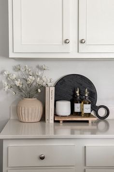 a white dresser topped with lots of bottles and candles next to a vase filled with flowers