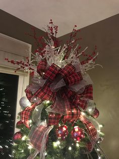 a christmas tree decorated with red and white plaid bows, lights and ornaments in a living room