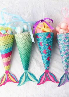 three little mermaid cones filled with marshmallows and candies are sitting on a white surface