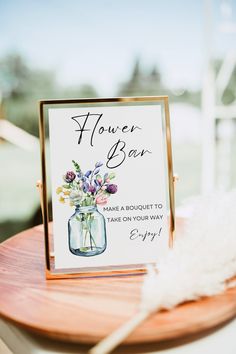 a flower bar sign sitting on top of a wooden table next to a white feather