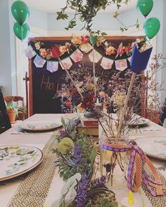 the table is set with plates, flowers and balloons