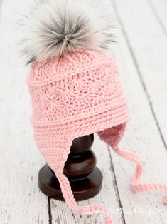 a pink knitted hat with a pom - pom on top, sitting on a wooden stand