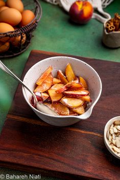 a bowl filled with fruit and nuts on top of a wooden cutting board next to bowls of eggs