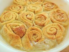 a white bowl filled with cinnamon rolls on top of a wooden table