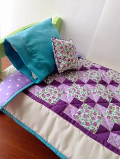 a bed with purple and green pillows on top of it next to a stuffed animal