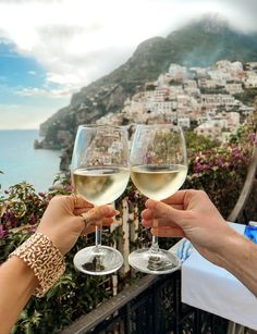 two people toasting with white wine in front of a view of the ocean and town