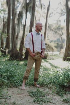 a man standing in the woods wearing suspenders