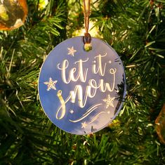 a blue ornament hanging from a christmas tree with the words let it snow on it