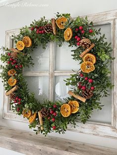 a wreath made out of oranges and pine cones hanging on a window sill