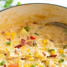 a pot filled with chicken and corn soup on top of a white tablecloth next to a wooden spoon