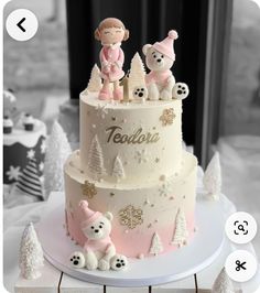 a white and pink cake with teddy bears on top, surrounded by snowflakes