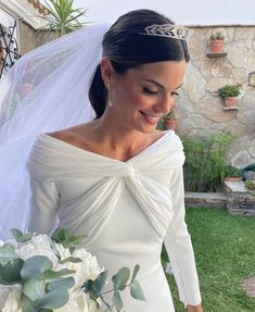 a woman wearing a wedding dress and veil holding a bouquet in her hand while looking at the camera