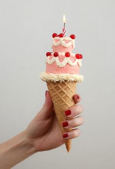 a hand holding an ice cream cone with a birthday cake on top and candles in it