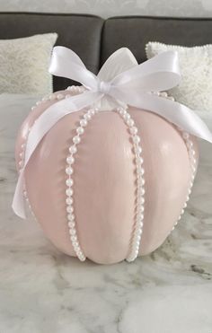 a pink pumpkin decorated with pearls and a white ribbon on top of a marble table