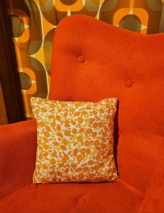 an orange chair with a pillow on top of it next to a wall covered in circles