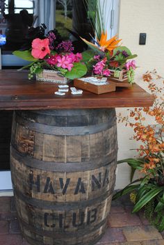 a wooden barrel sitting on top of a brick floor next to flowers and plants in front of a building