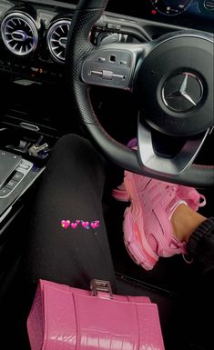 a pink purse sitting on top of a car floor next to a steering wheel and dashboard