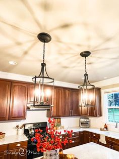 a kitchen with two chandeliers hanging from it's ceiling and wooden cabinets