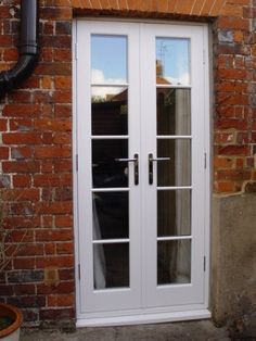 a white double door sitting next to a red brick wall and potted plant in front of it