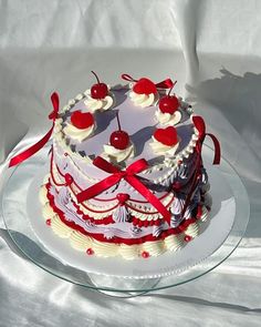 a white cake with cherries on top and ribbons around the edges is sitting on a glass platter