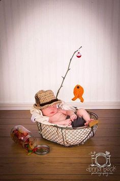 a baby wearing a hat and sitting in a basket next to an orange fish ornament