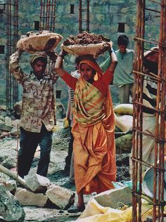 two women carrying items on their heads while walking through the rocks and rubbles behind them