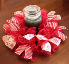 a red and white christmas wreath sitting on top of a wooden table next to a jar