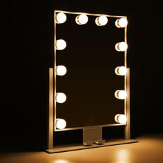 a lighted mirror with bulbs on it in the middle of a dark room and black background