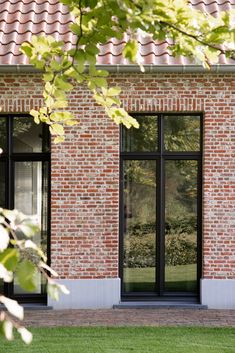 a brick building with two large windows next to a grassy area and trees in the background