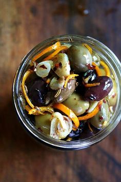 a glass jar filled with olives and orange peels on top of a wooden table