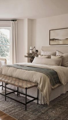 a bedroom with a bed, bench and windows in the room that has white walls