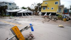 a street sign laying in the sand next to houses that have been torn down by strong winds