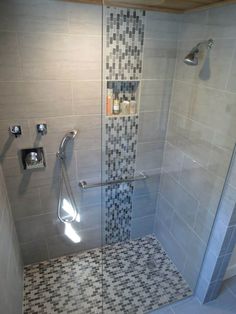 a walk in shower sitting next to a tiled wall and white tile floor with black and gray tiles on the walls