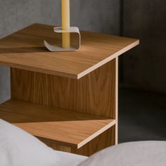 a candle is sitting on top of a wooden shelf next to a white bed sheet