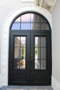 a black double door with two sidelights and arched glass on the front of a house