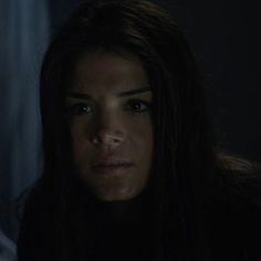 a woman with long dark hair stares into the distance in a dimly lit room at night