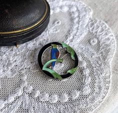 Featuring an amazing antique Victorian/Arts and Crafts signed sterling silver brooch adorned with a blue, green and red enamel bird surrounded by brilliant mint and sap green enamel leaf accents on a circular black enamel sterling ring.  Brooch is in excellent antique condition with functional antique fold over clasp, enamel is just gorgeous with no wear noticeable.  Brooch measures approximately 3 centimeters in diameter at 5.9 grams.  The luminous quality of fine enamel work is mesmerizing, es Green Round Brooch For Gift, Green Round Brooches For Gift, Round Enamel Brooches As Gift, Vintage Round Enamel Pin For Gift, Sap Green, Sterling Silver Brooch, Victorian Art, Silver Brooch, Green Enamel