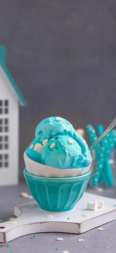 a cupcake with blue frosting and sprinkles on it sitting in front of a doll house