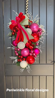 a wreath hanging on the front door decorated with red and pink ornaments, bows and baubles