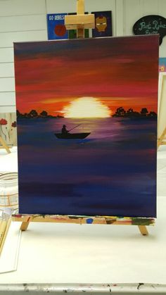 an easel with a painting on it in the shape of a boat at sunset