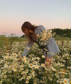 a woman kneeling down in a field of daisies