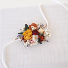 a bridal bouquet with dried flowers and white ribbon on a bed sheet in the sunlight