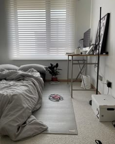 an unmade bed sitting next to a window in a room with blinds on the windowsill