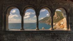 an old stone building with arches overlooking the ocean and cliffs in the distance, taken from inside one of the buildings